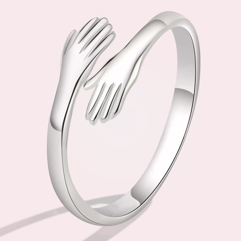Fijne zilveren handen omcirkelen deze ring, en creëren een ontwerp dat nabijheid en warmte symboliseert