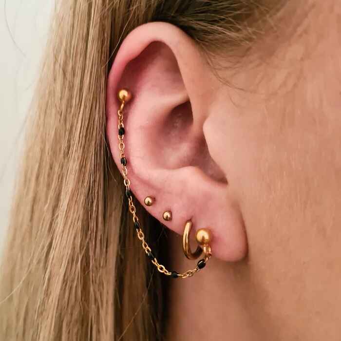 Een glinsterende gouden ketting bezaaid met zwarte accenten hangt tussen de studs, ontworpen om helix piercings te verheffen met verfijnde schoonheid