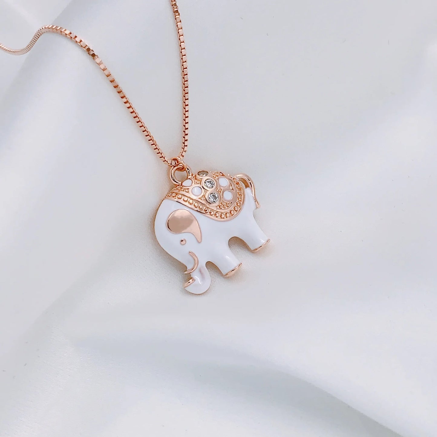 Een stralend gouden olifant-bedeltje, met een rug bedekt met een saffierkleurig geëmailleerd kleed, dat de harmonieuze balans tussen kracht en sereniteit weerspiegelt
