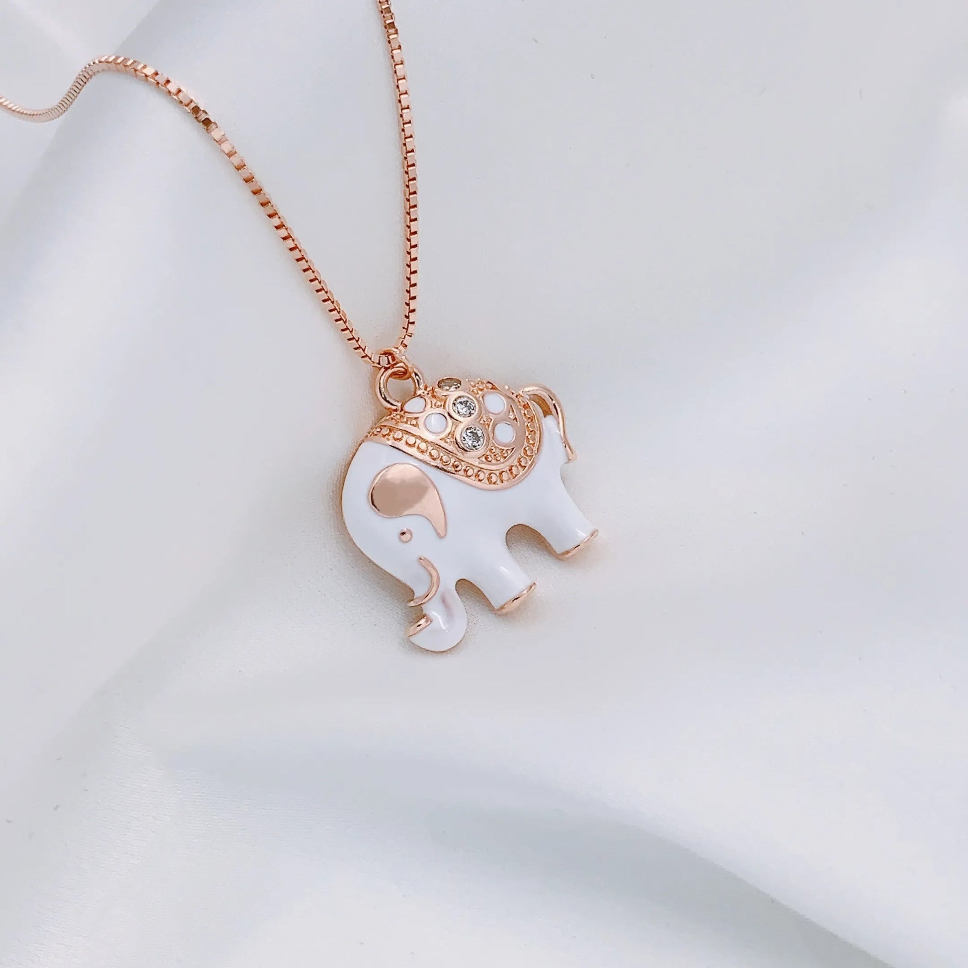 Een stralend gouden olifant-bedeltje, met een rug bedekt met een saffierkleurig geëmailleerd kleed, dat de harmonieuze balans tussen kracht en sereniteit weerspiegelt
