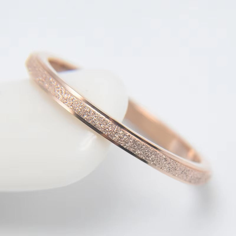 Een slanke rosegouden band toont zowel geborstelde als glanzende texturen, die het licht weerkaatsen in een subtiele schittering